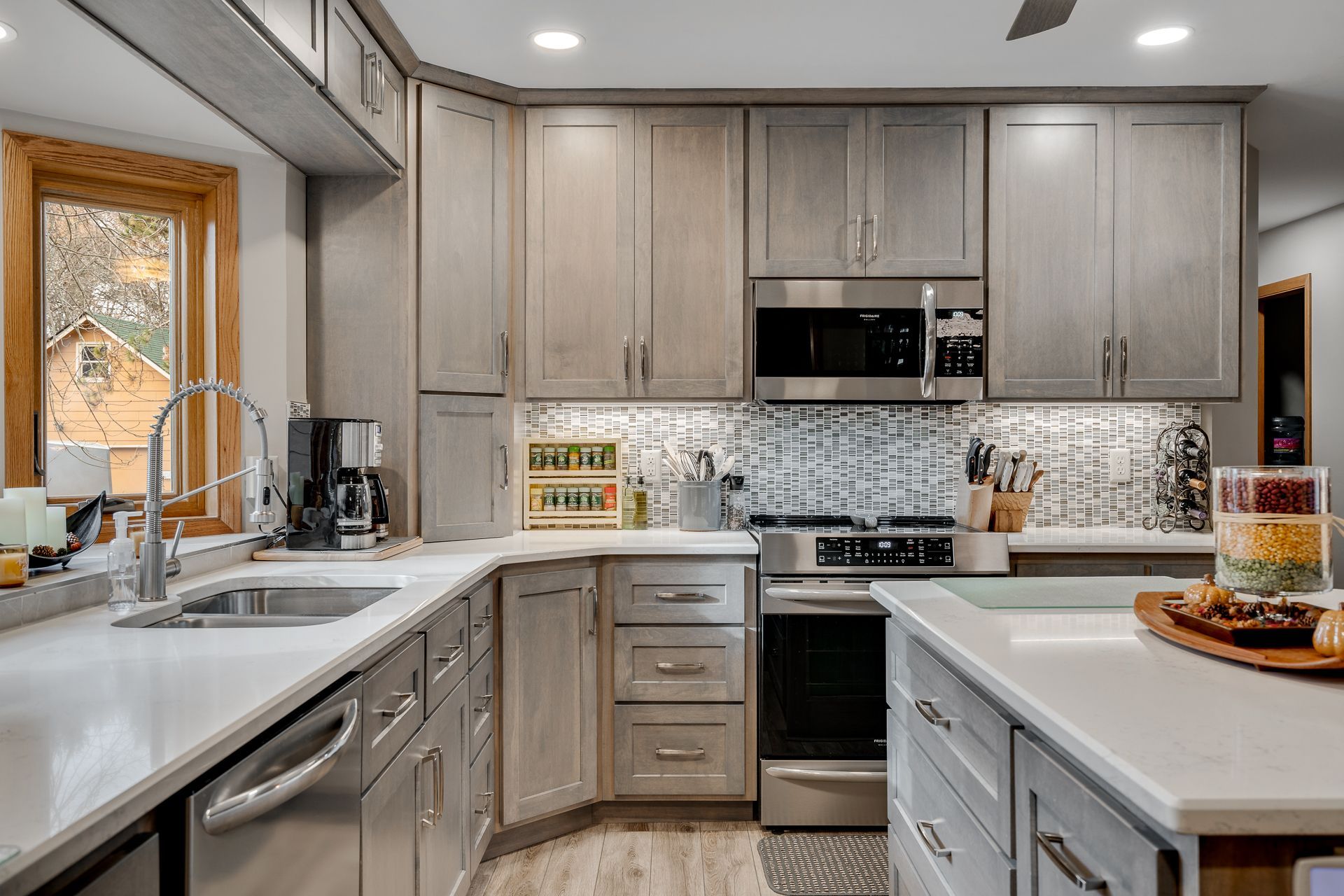 Modern kitchen with gray cabinets, white countertops, stainless steel appliances, and a mosaic backsplash.