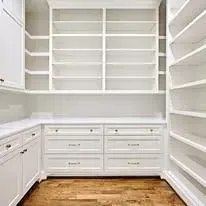A walk in closet with white cabinets, drawers, and shelves.