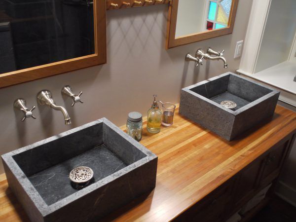 Two gray rectangular sinks on a wood counter with silver faucets, mirrors, and toiletries.