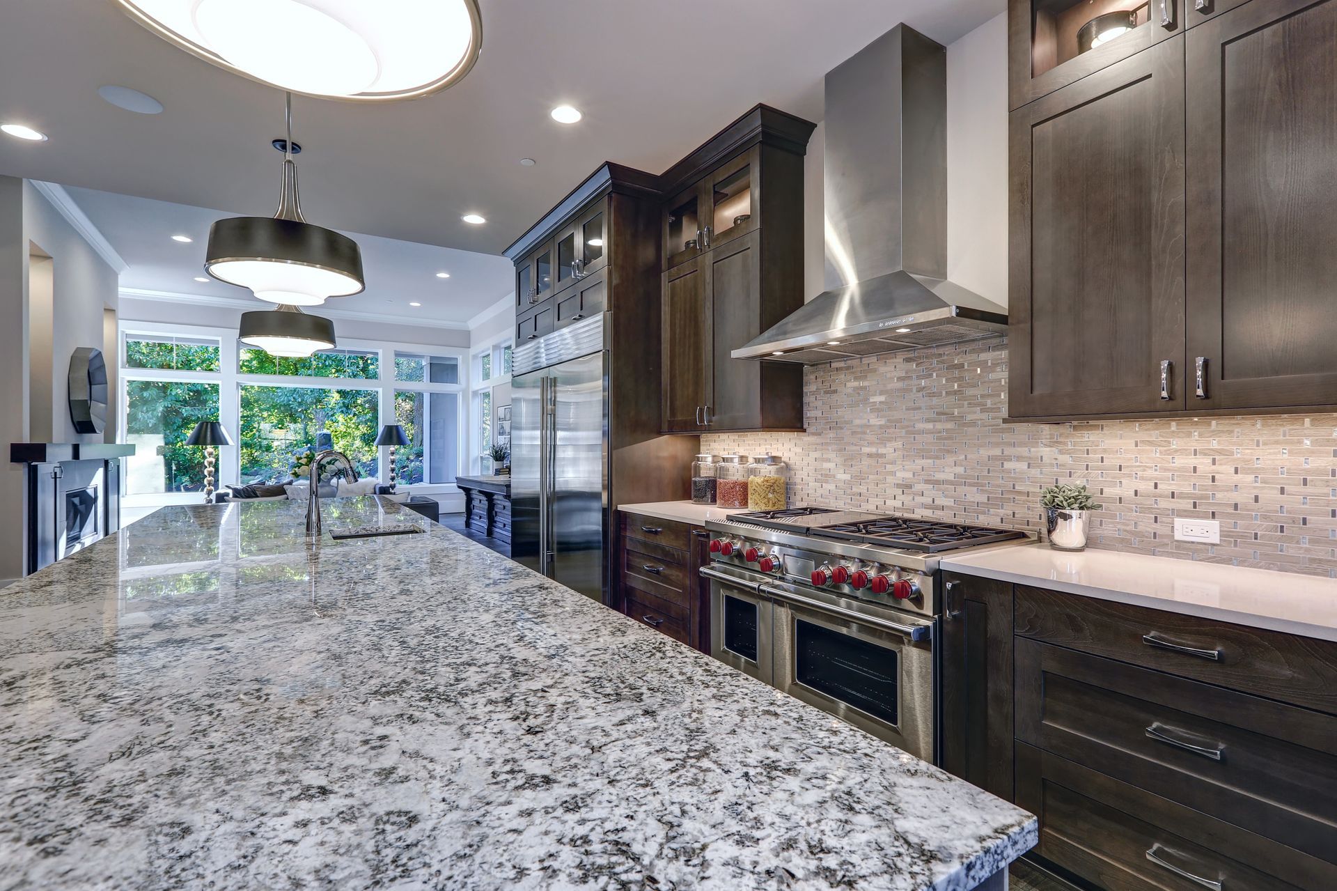 Modern kitchen with large island, stainless steel appliances, dark wood cabinets, and granite countertops.