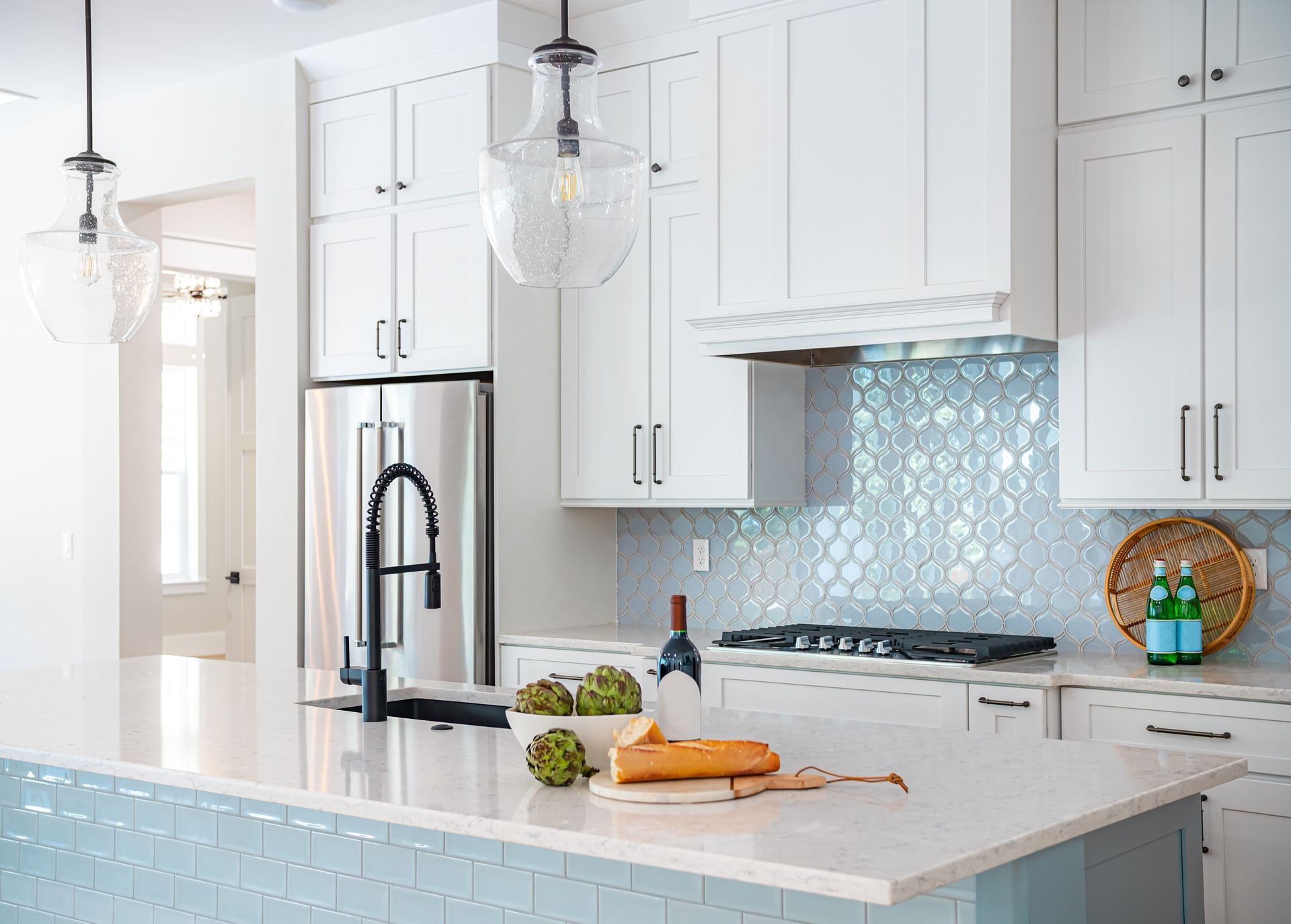 White kitchen with blue tiled backsplash and island, stainless steel appliances, and pendant lighting.