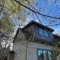 A house with a roof that has a window on it surrounded by trees.