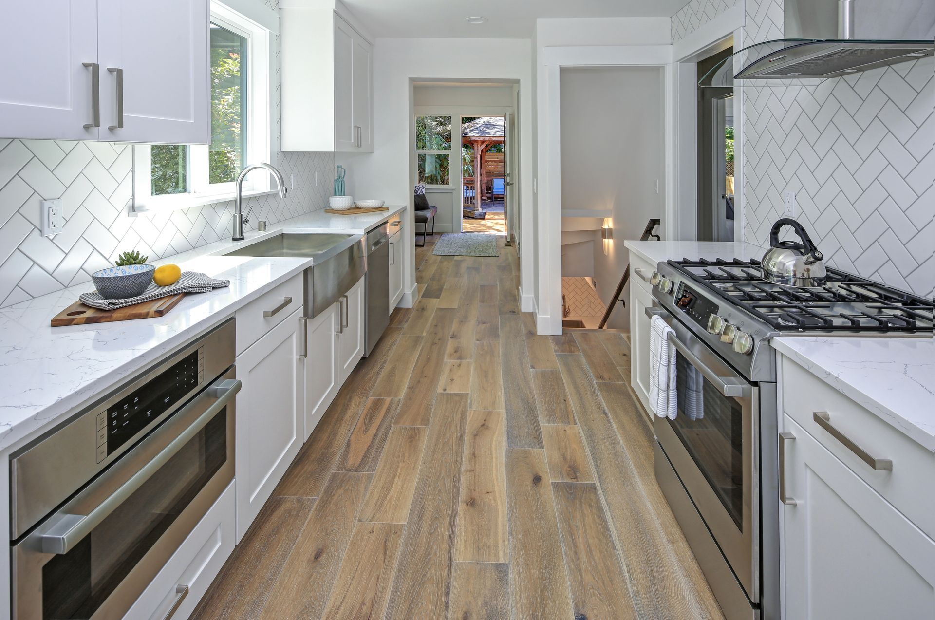 Modern, white kitchen with stainless steel appliances, herringbone backsplash, and wood floor.