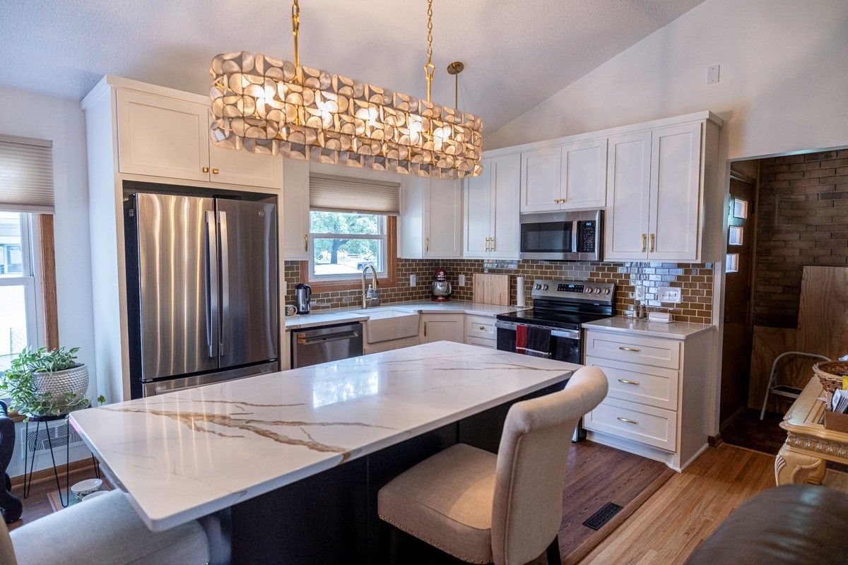 Modern white kitchen with island, stainless steel appliances, and a decorative light fixture.