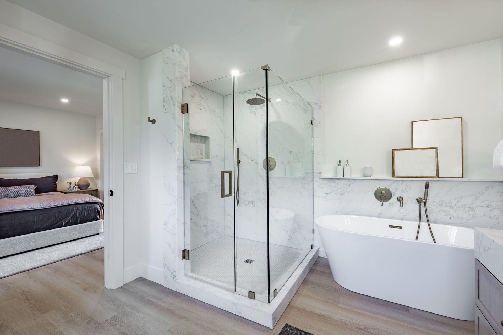 Modern bathroom with glass shower, soaking tub, and view into bedroom. White and marble accents.