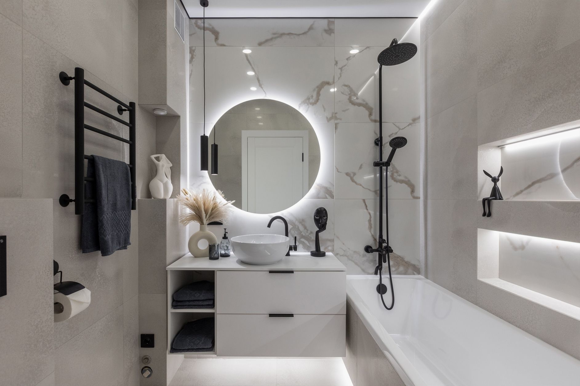 Modern bathroom with marble-look wall, round mirror with lights, black fixtures, and a white bathtub.