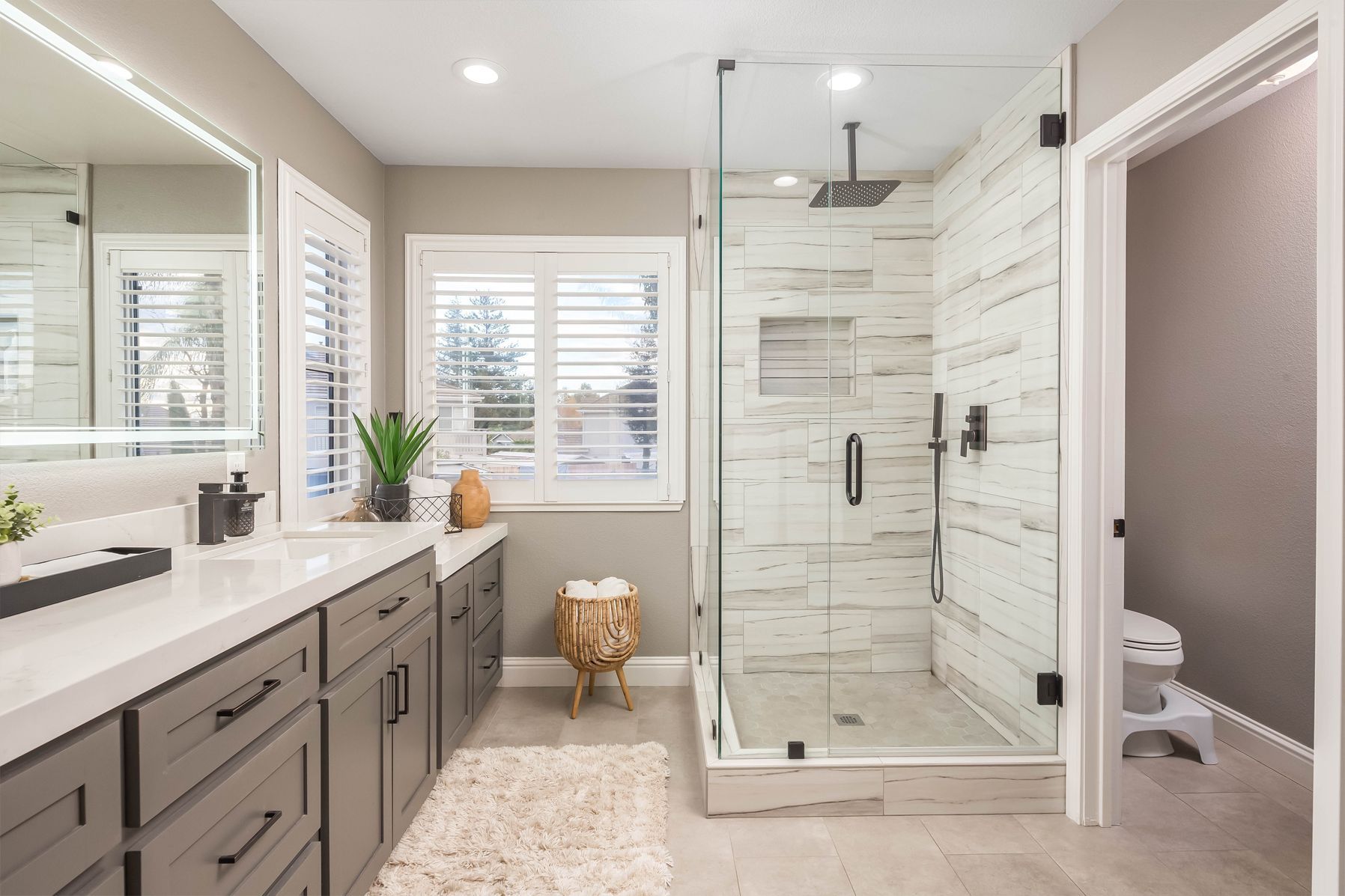 Modern bathroom with gray cabinets, white countertops, glass shower, and white tiled walls.