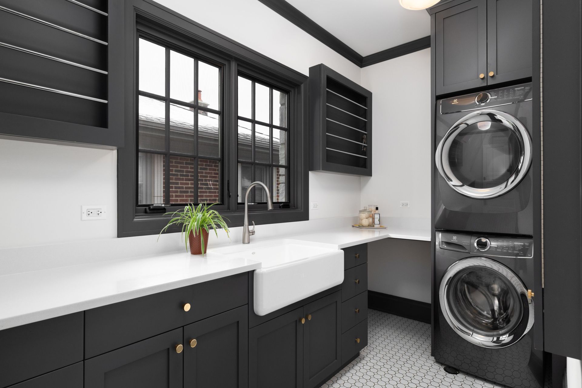 Laundry room with black cabinets, white countertop, window, stacked washer/dryer, and sink.