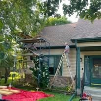 A man is standing on a ladder painting the roof of a house.