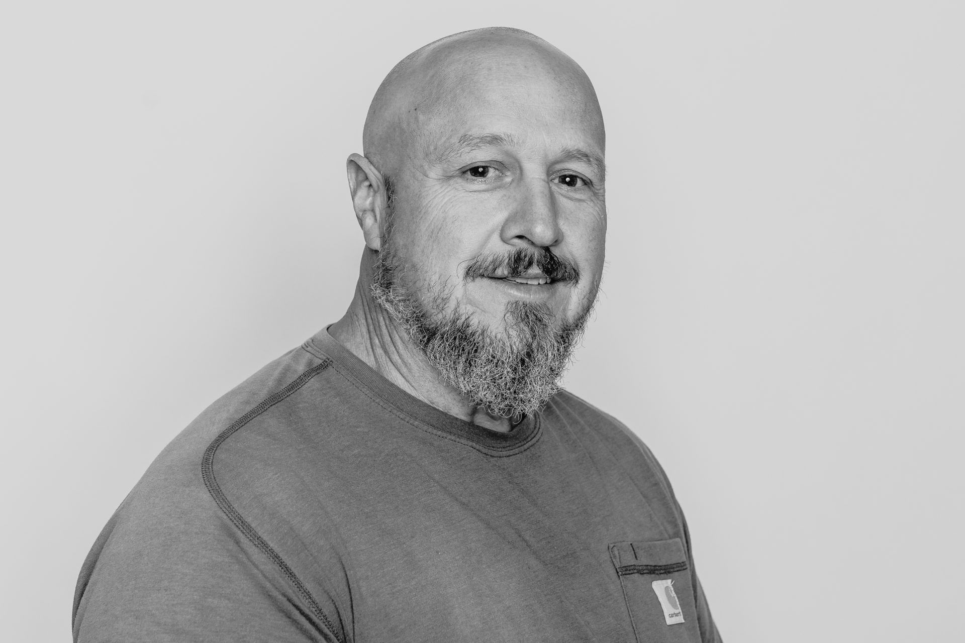 Black and white portrait of a person with a beard wearing a crew neck shirt, looking toward the camera.
