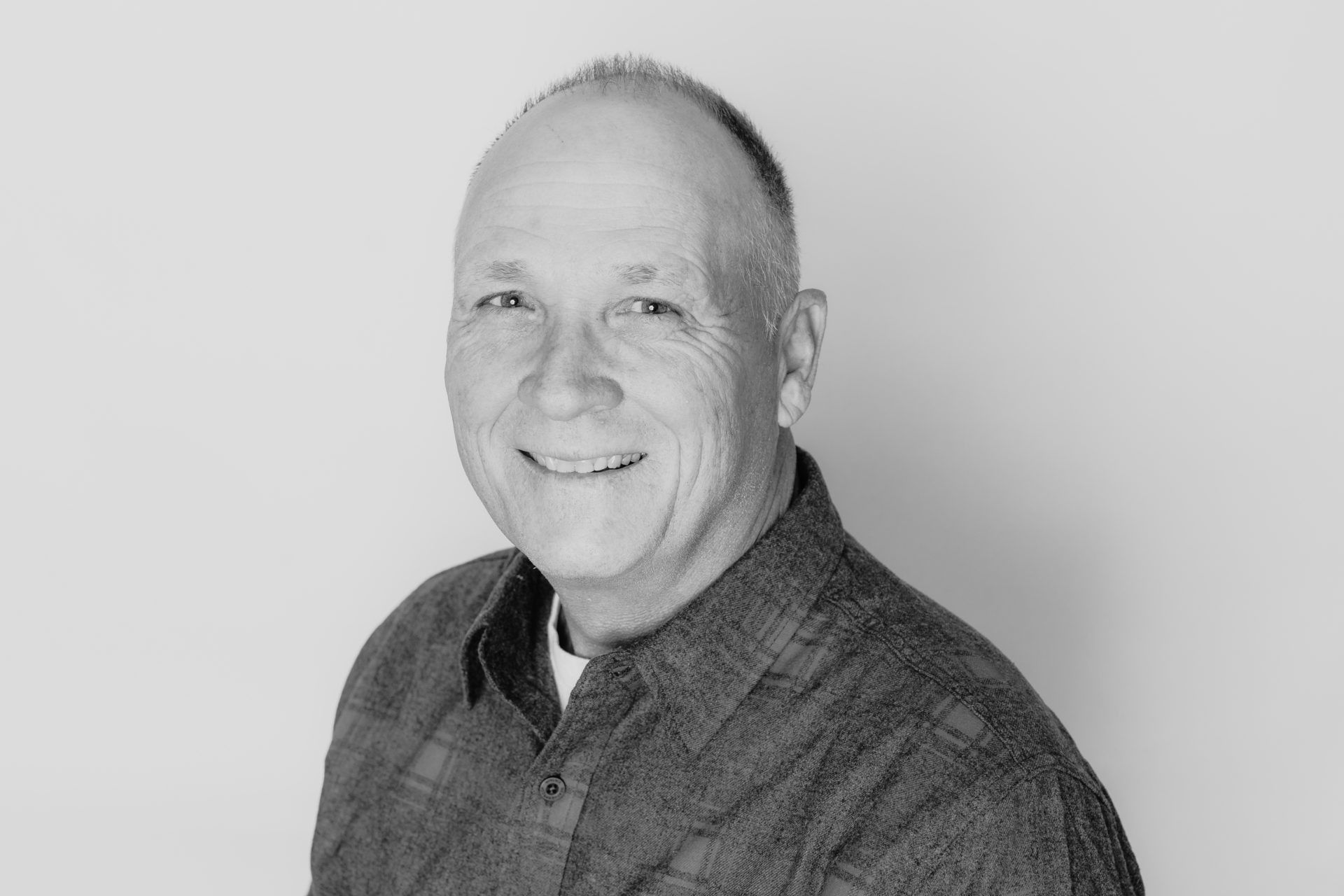 A head-and-shoulders portrait of a smiling person in a button-down shirt against a plain, light background.
