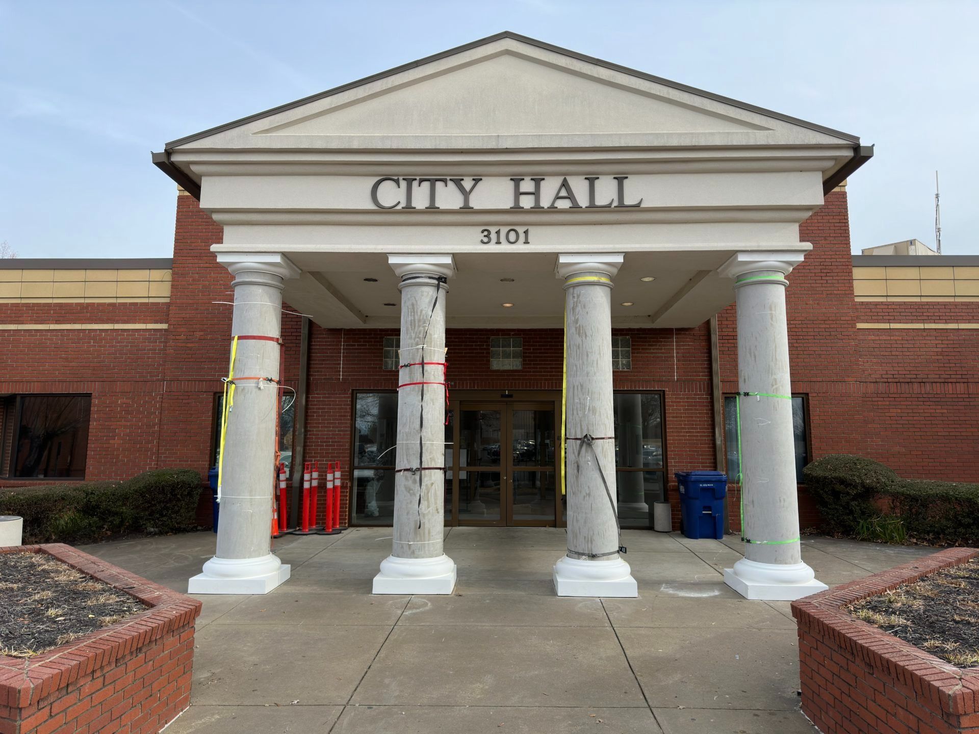 The entrance to a red-brick City Hall building with a white triangular pediment supported by four light-colored columns.