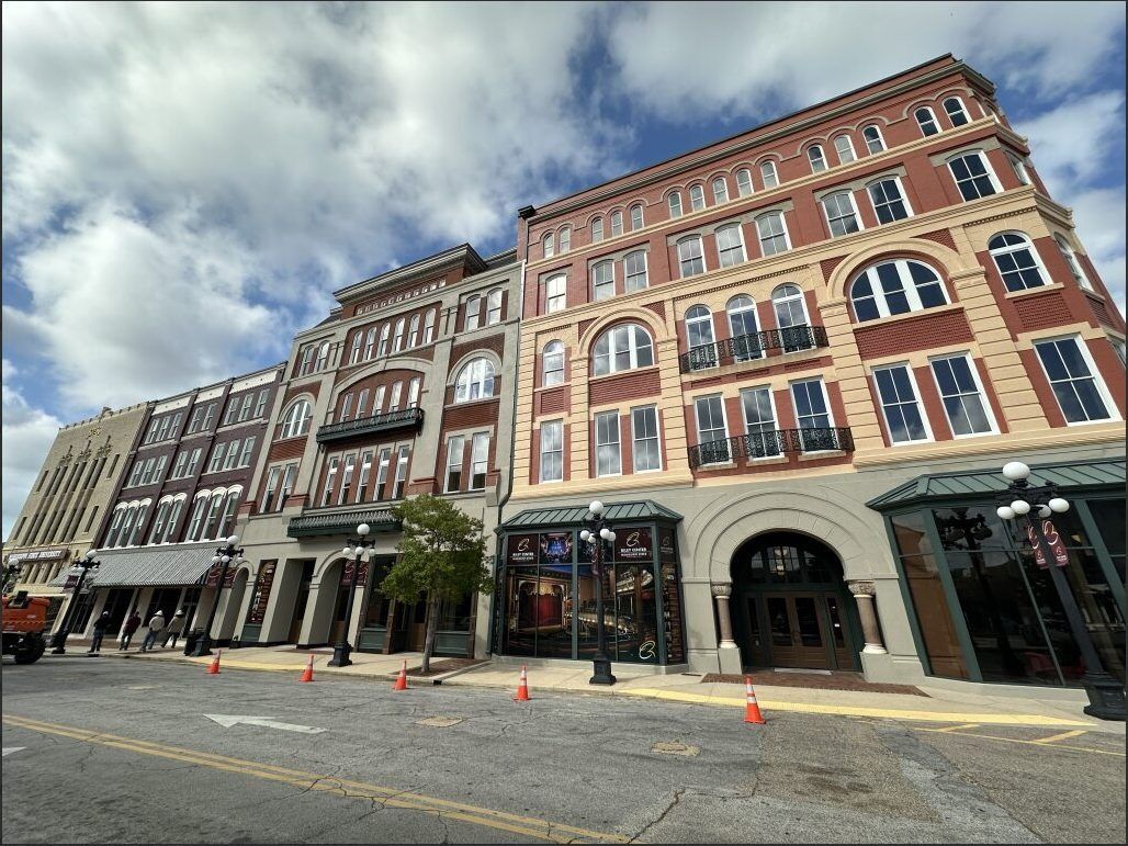 A street-level view of ornate, multi-story brick buildings with arched windows lining a city street under a cloudy sky.