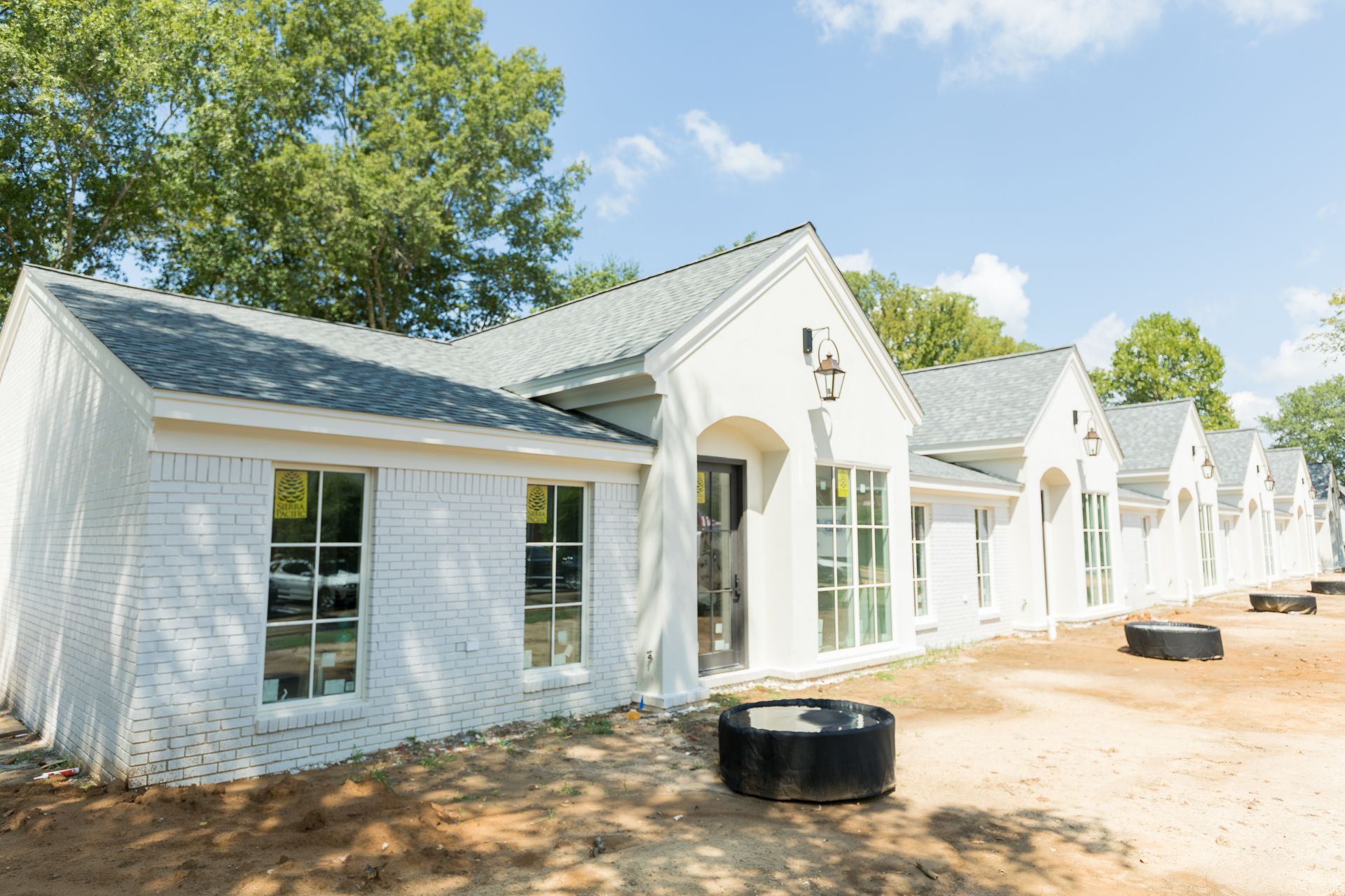 A row of newly constructed white, brick-style homes with grey shingled roofs against a blue sky.