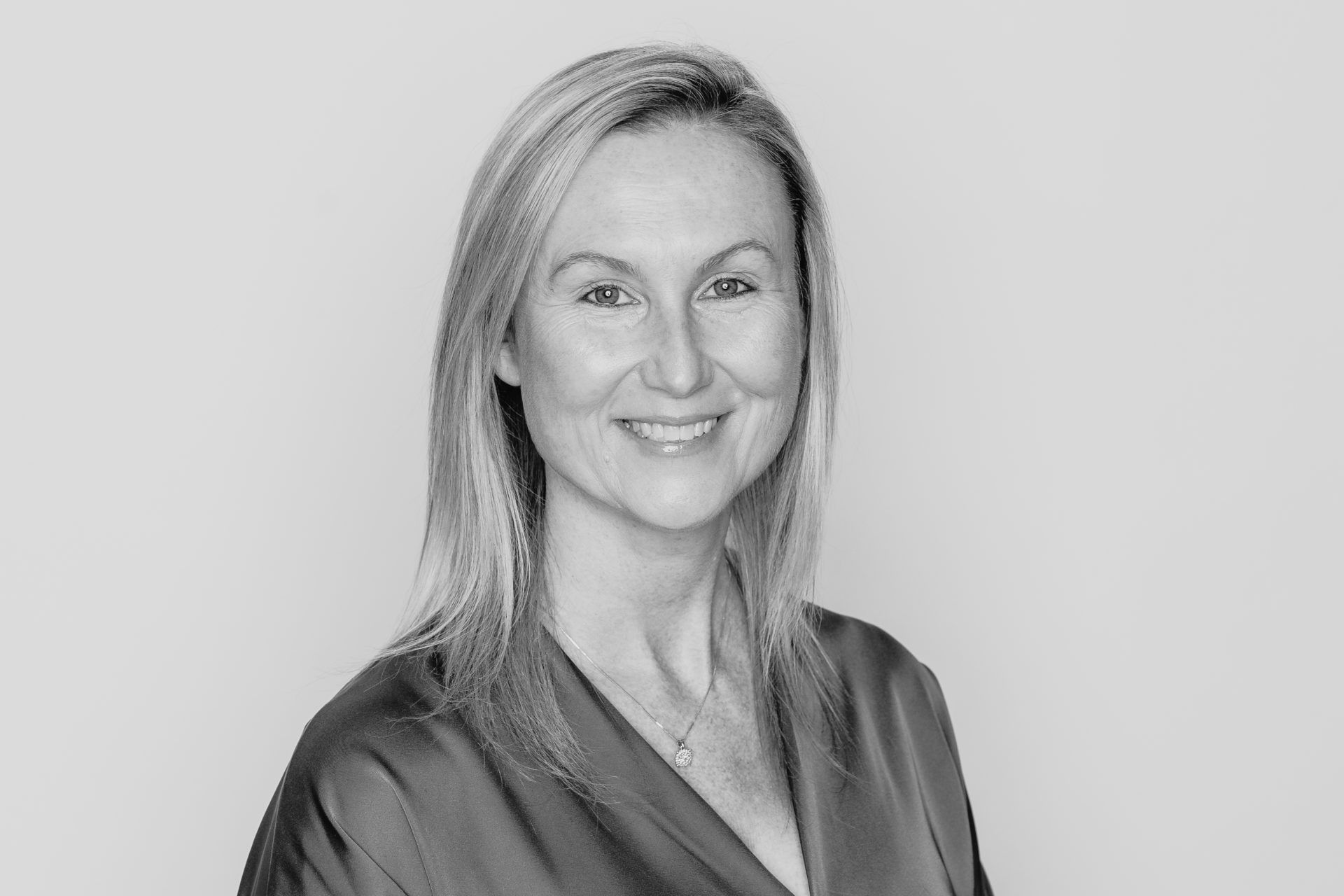 Headshot of a smiling person with shoulder-length hair wearing a collared shirt against a plain, light background.