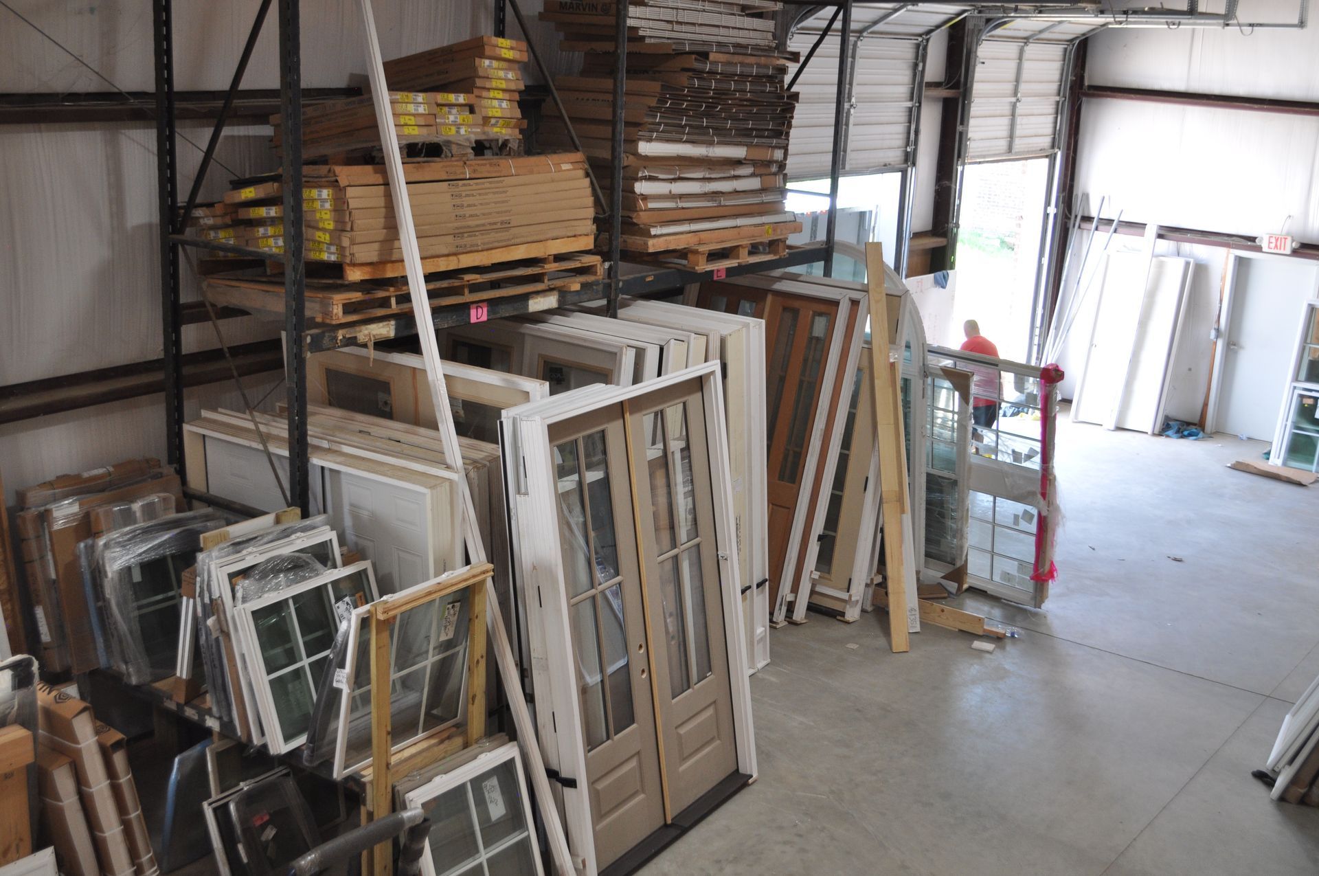 Warehouse interior filled with stacks of wooden boards, various windows, and doors, with a worker visible in the back.
