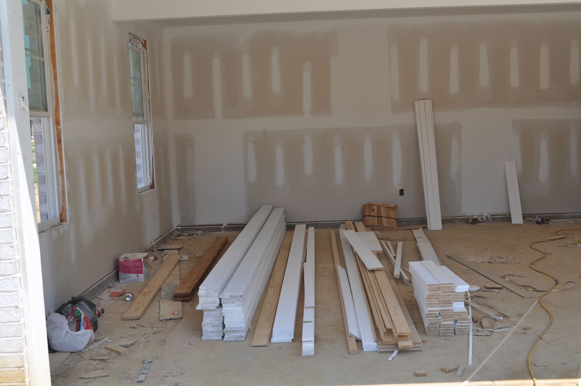 An interior view of a room under construction with unfinished drywall, stacked baseboards, and construction materials.