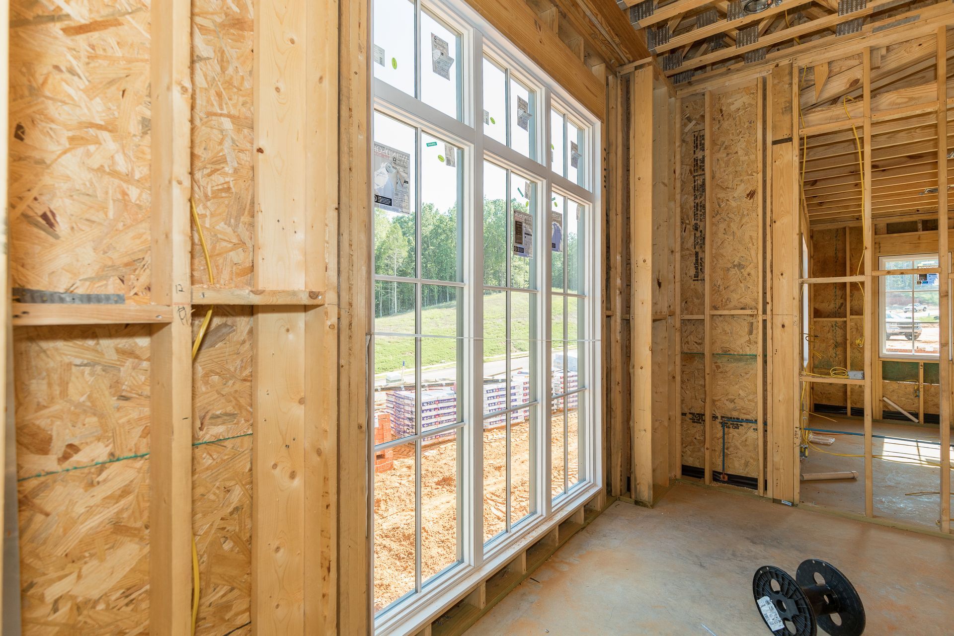 Interior view of a residential construction site featuring framed wooden walls and a large, newly installed window.