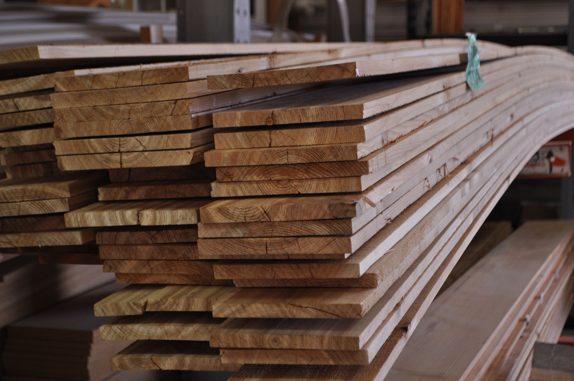 A stack of long, light-brown wooden boards piled in a warehouse setting.