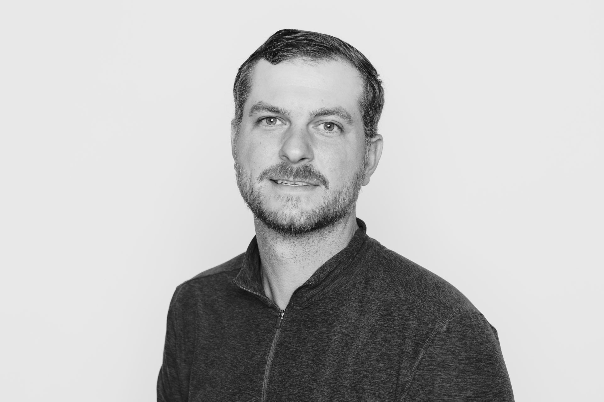 A person with short, dark hair and a mustache wearing a dark sweater against a plain, light-colored background.