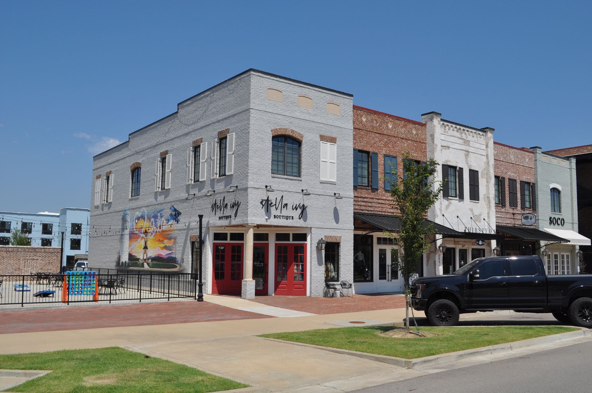 A two-story brick corner building with red-framed entrances, a mural, and a black pickup truck parked in front.