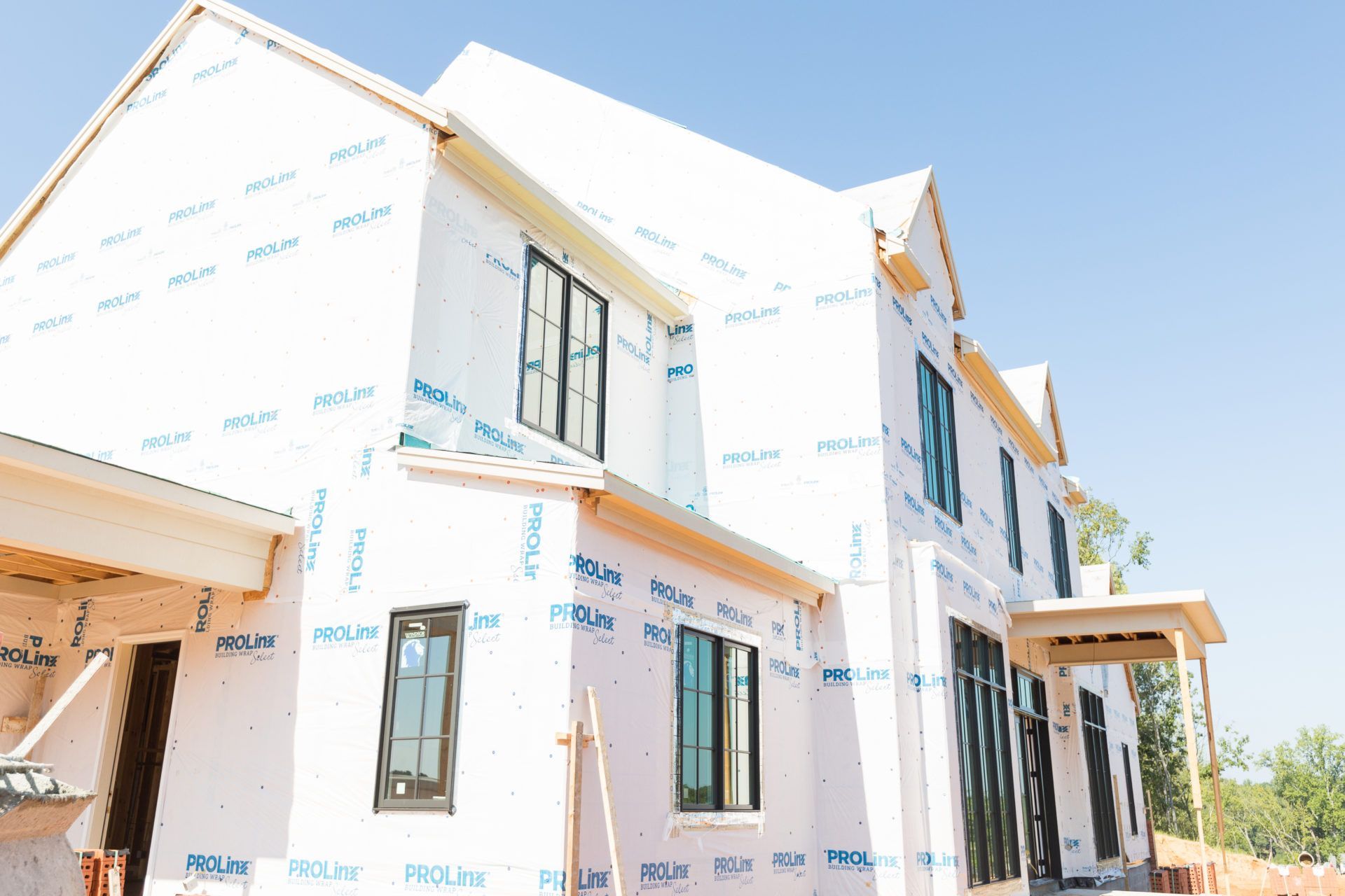 New houses under construction with white wrap and black-trim windows in a sunny neighborhood