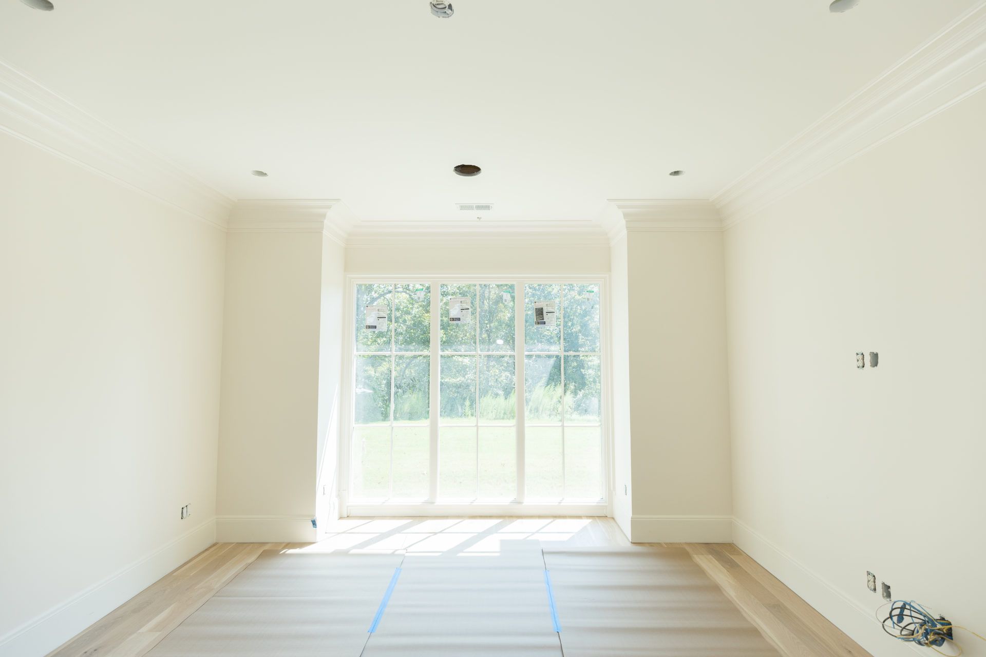 Empty bright room with white walls, wood floor, and large sliding glass doors to a backyard.
