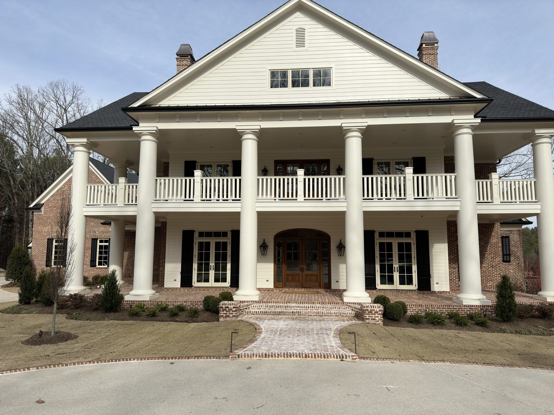 Large two-story white colonial house with tall columns, black shutters, and a wraparound porch