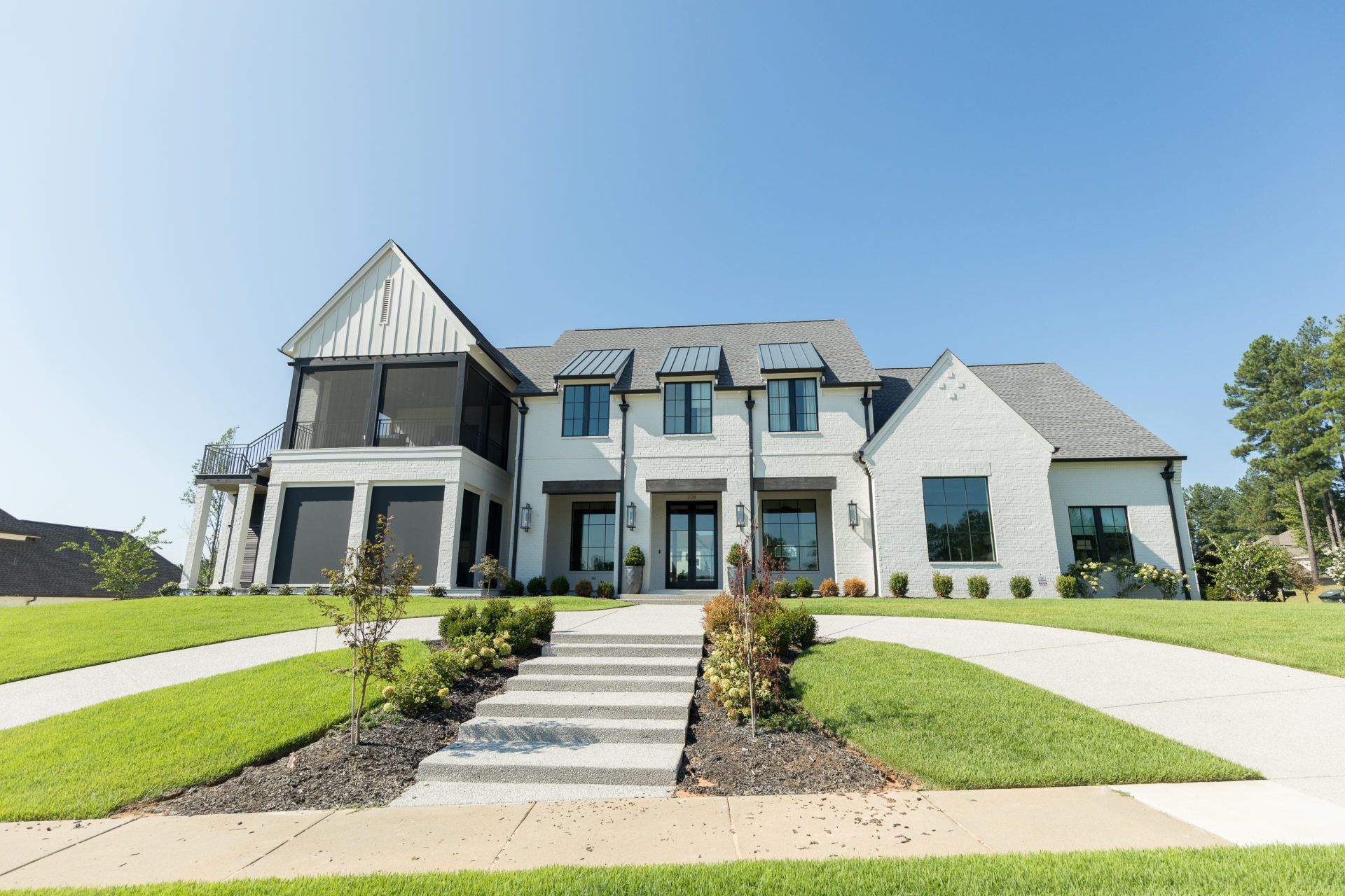 Large modern suburban house with white and gray exterior, front steps, and manicured lawn under a clear blue sky