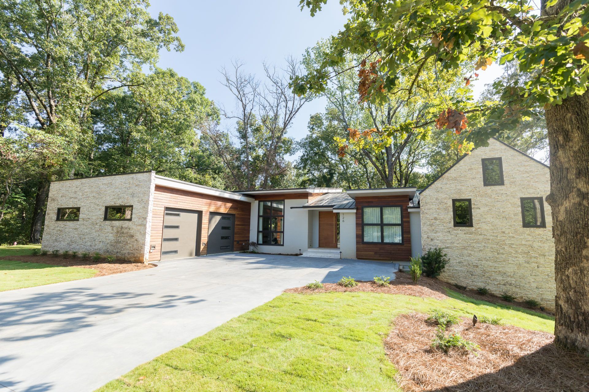 Single-story brick house with a two-car garage, front lawn, and large trees in the yard