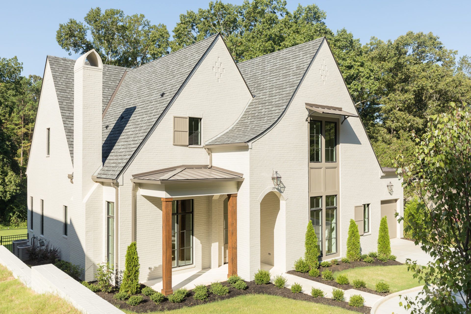 Modern white house with steep gabled roofs, arched entryway, and landscaped front yard