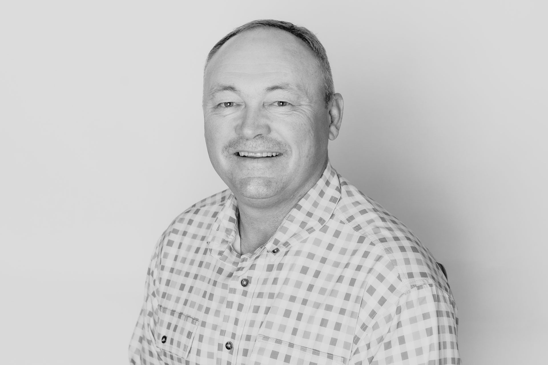 A smiling person wearing a patterned button-down shirt against a plain, light background.