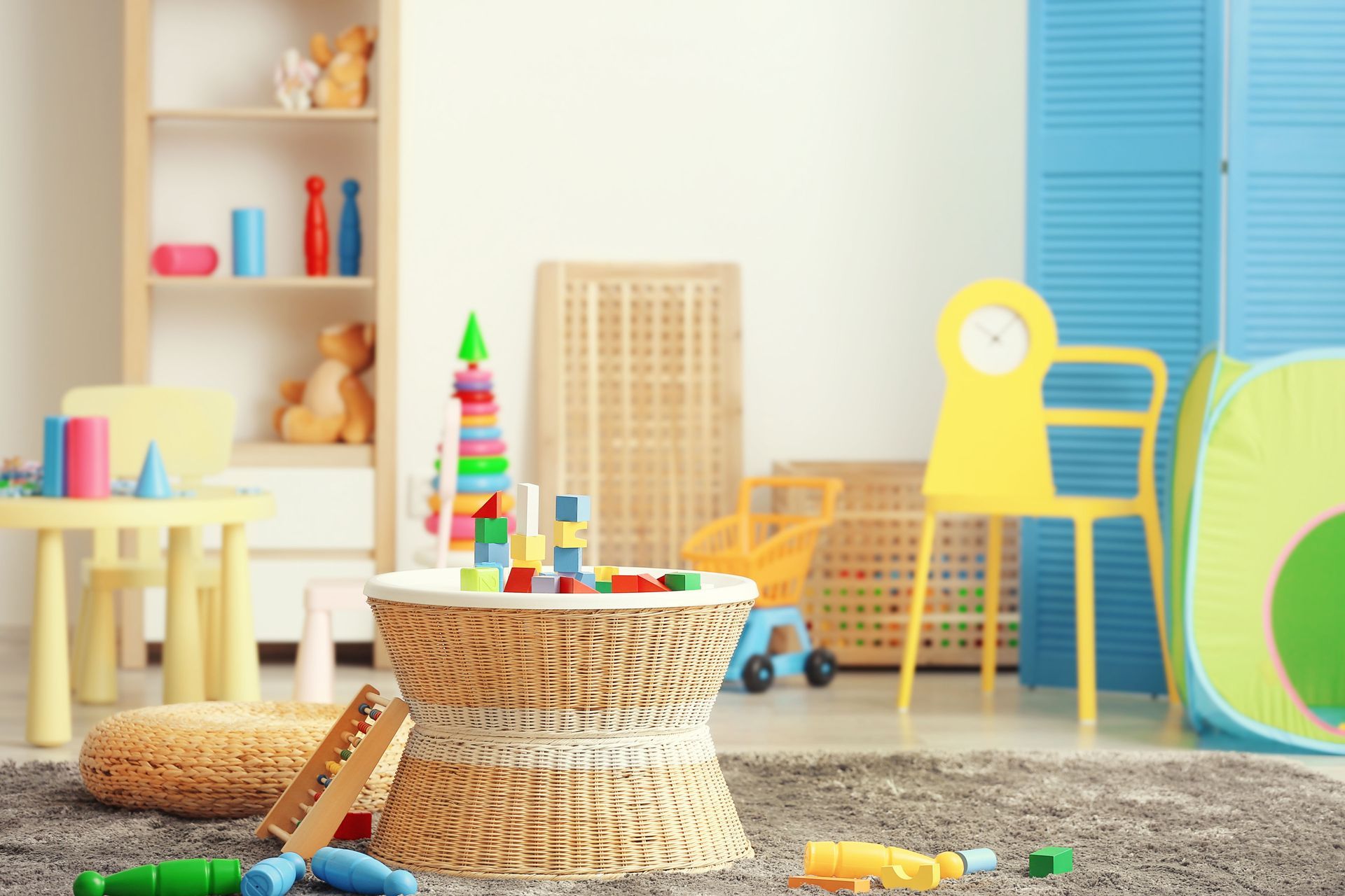 Playroom with toys on a rug, table, and shelves; light blue, yellow, and brown tones.