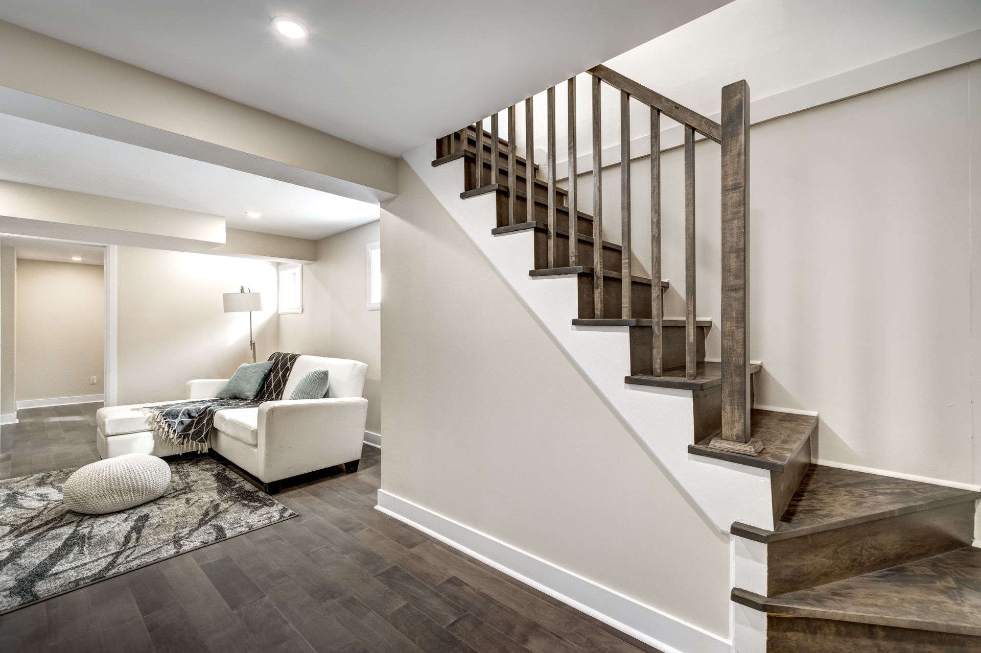 Dark wooden stairs with a wooden railing leading to a living room with a white couch and dark wood floor.