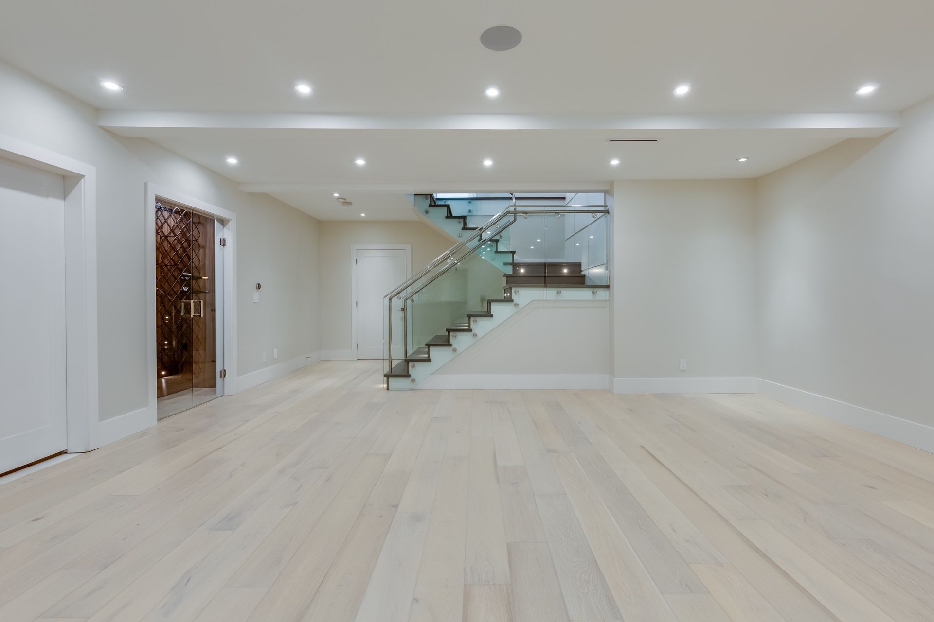 Empty room with hardwood floors, recessed lighting, and a staircase with glass panels.