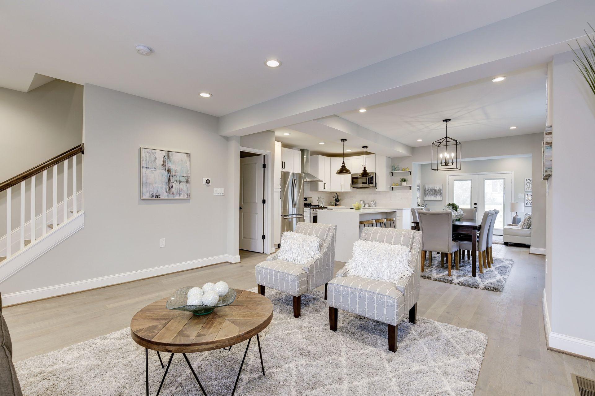 Open-concept living space with light wood floors, gray walls, kitchen, dining area, and staircase.