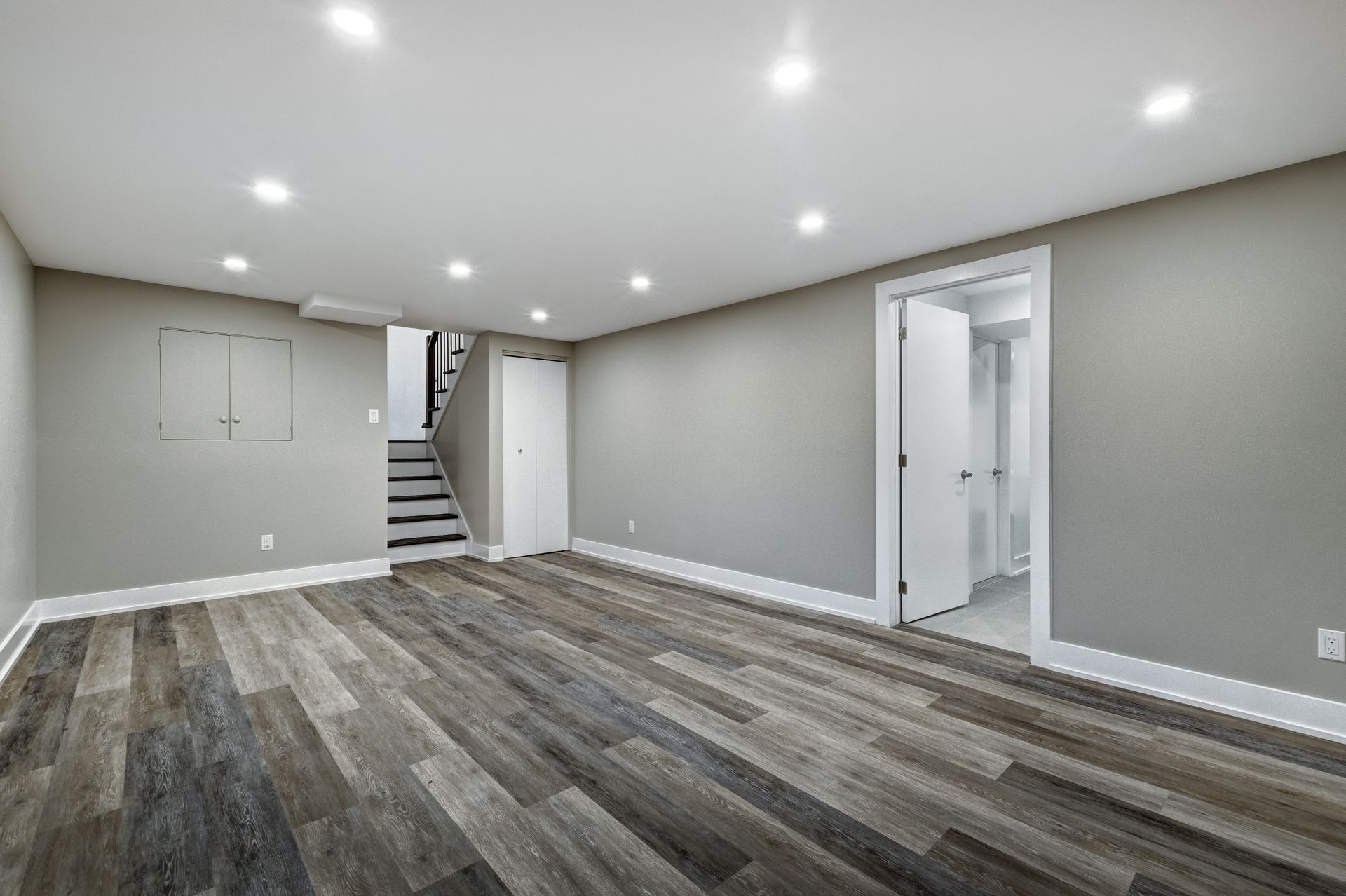 Empty, recently renovated basement with gray walls, wooden flooring, and recessed lighting.