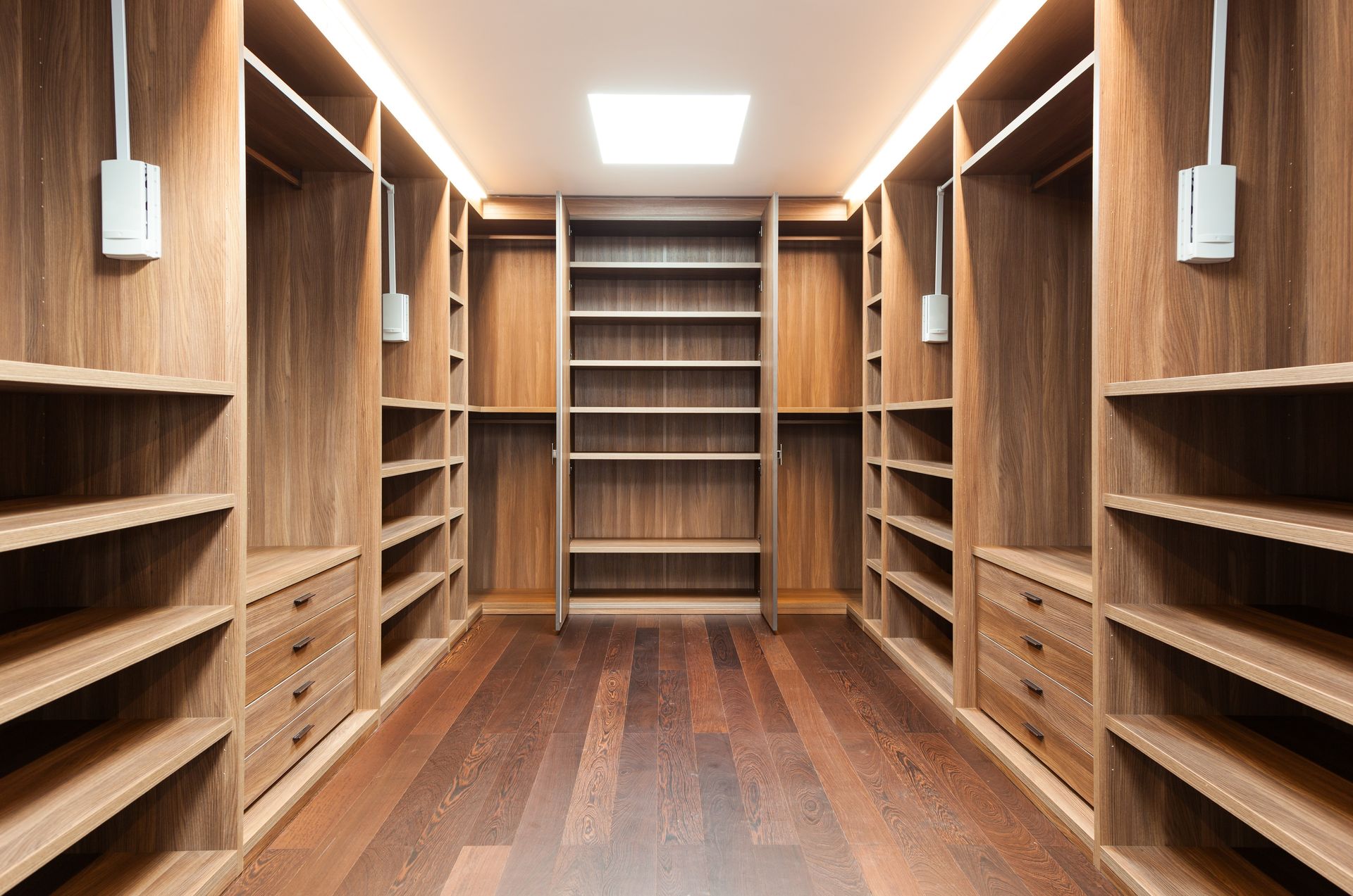 Empty walk-in closet with wooden shelves, drawers, and flooring. Recessed ceiling light.