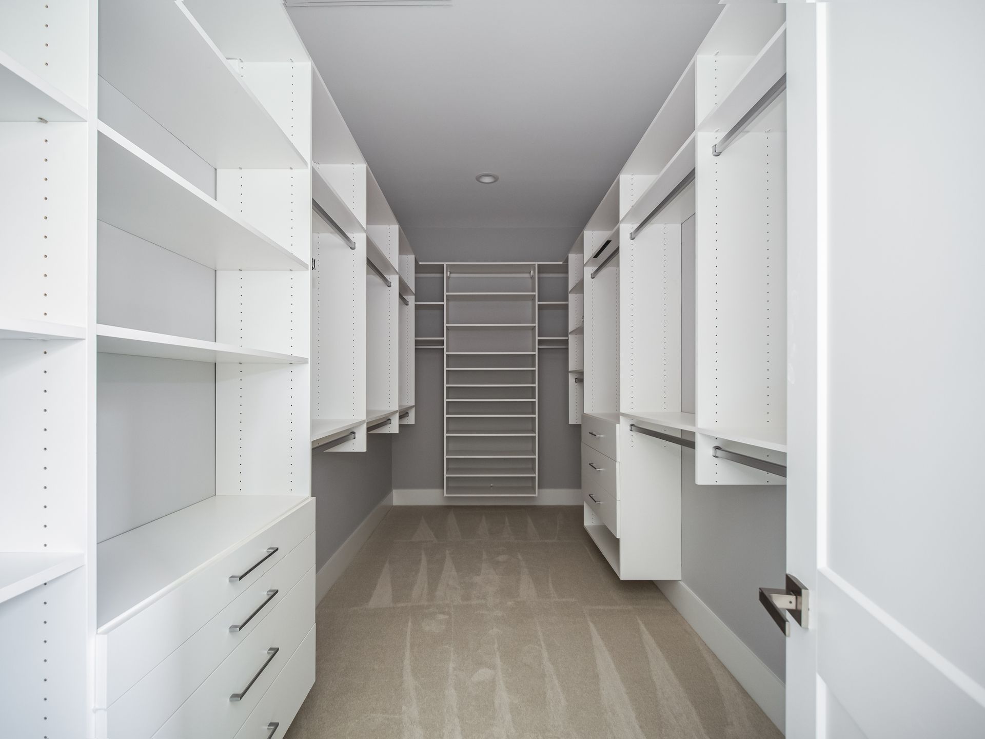 Walk-in closet with white shelving and drawers, gray walls, and tan carpet.