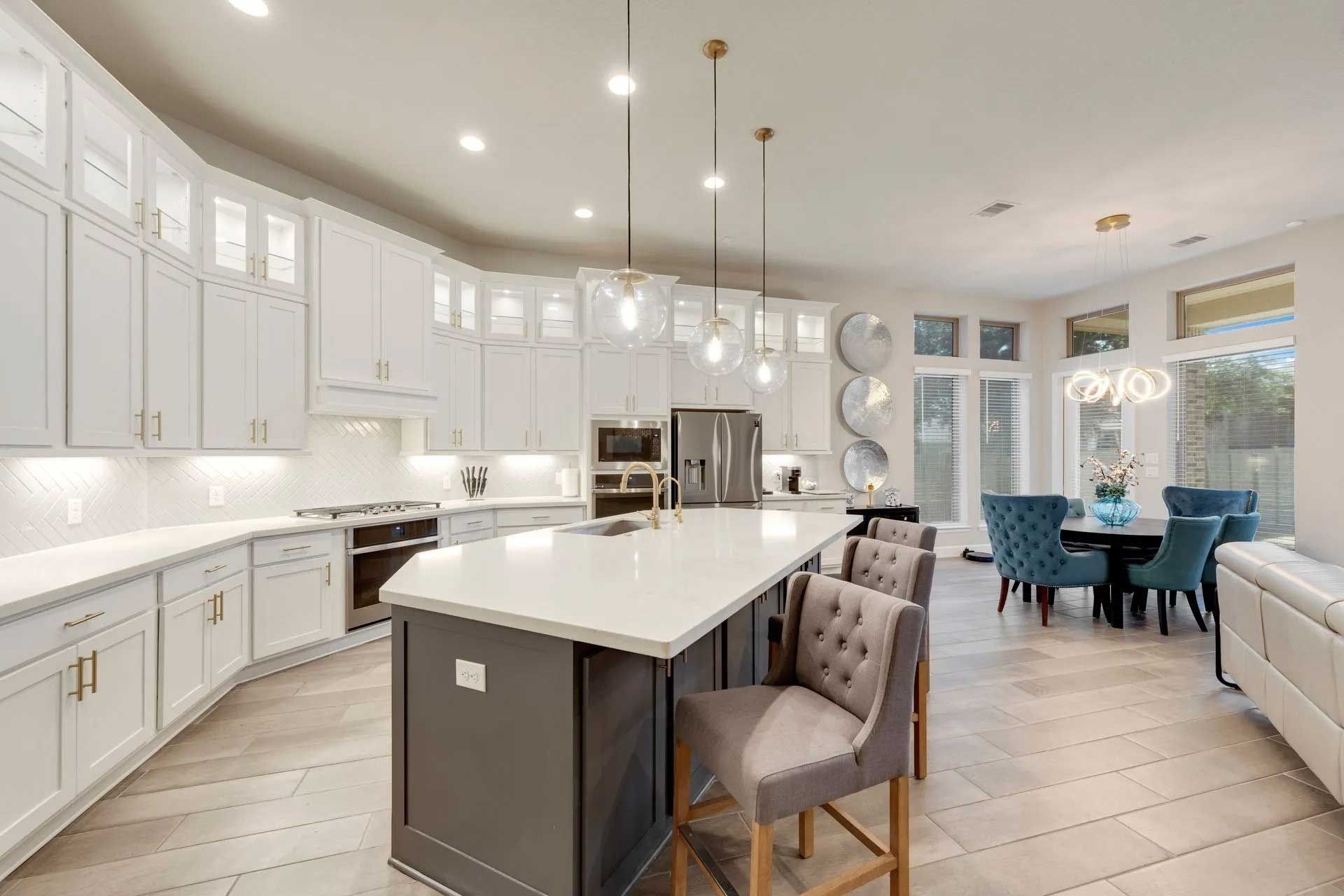 Modern kitchen with white cabinets, gray island, and blue dining chairs.
