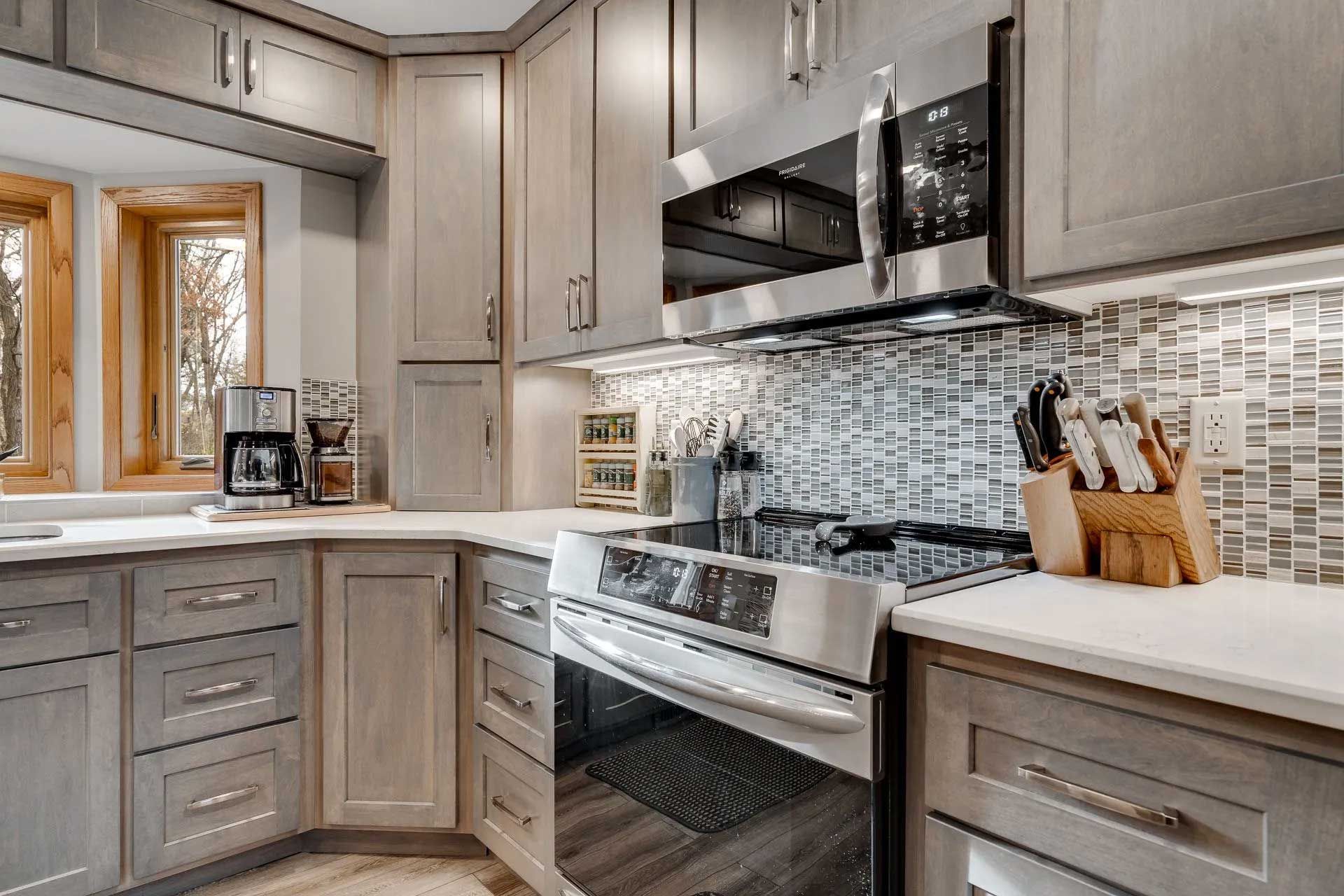 Modern kitchen with gray cabinets, stainless steel appliances, and mosaic backsplash.