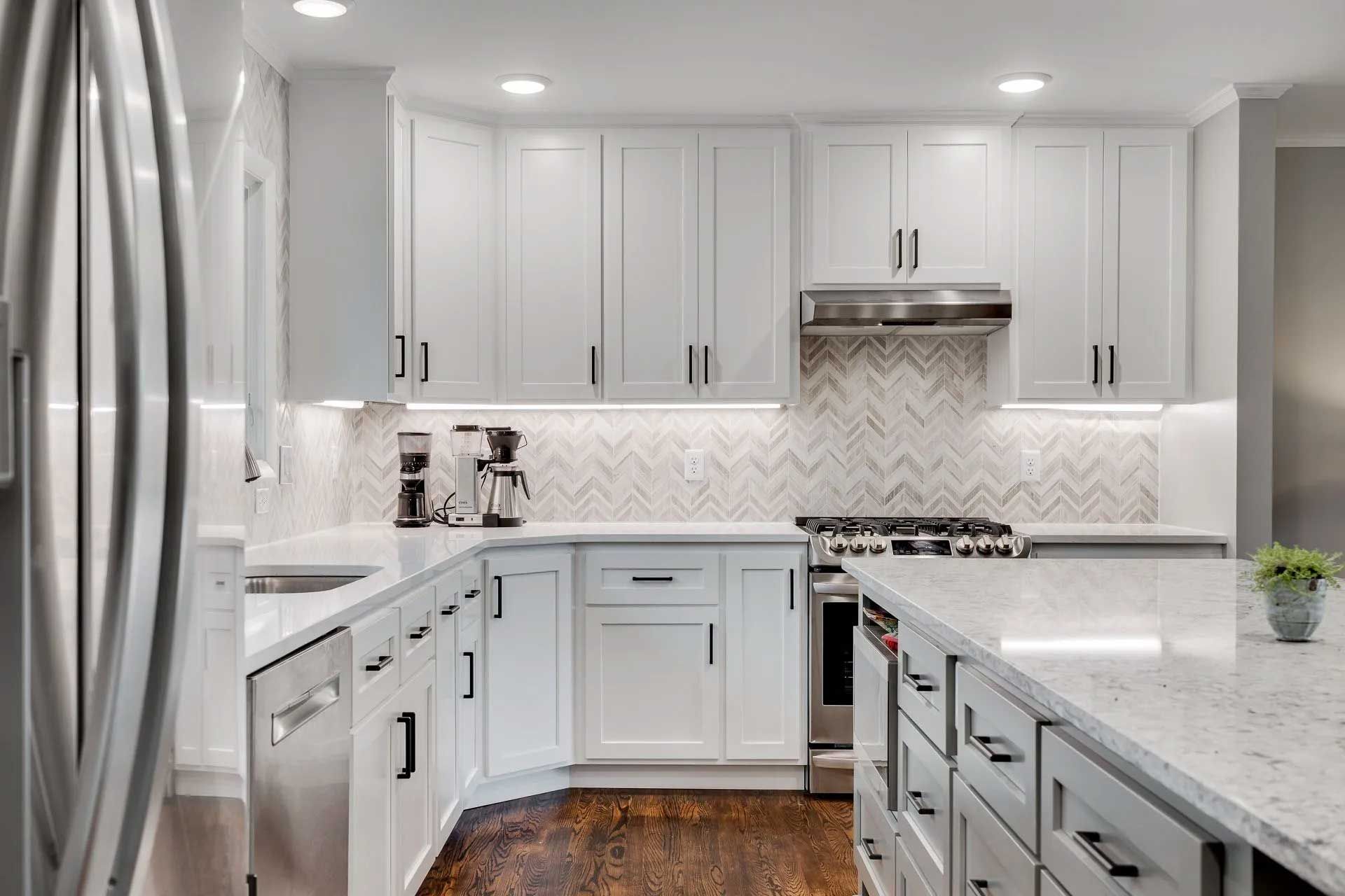 Modern white kitchen with stainless steel appliances, white cabinets, and a chevron backsplash.