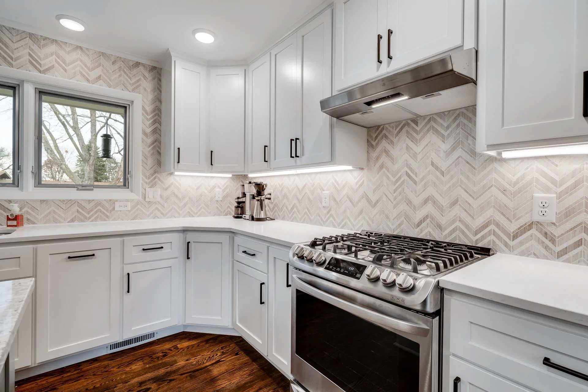 White kitchen with stove, cabinets, and herringbone backsplash.