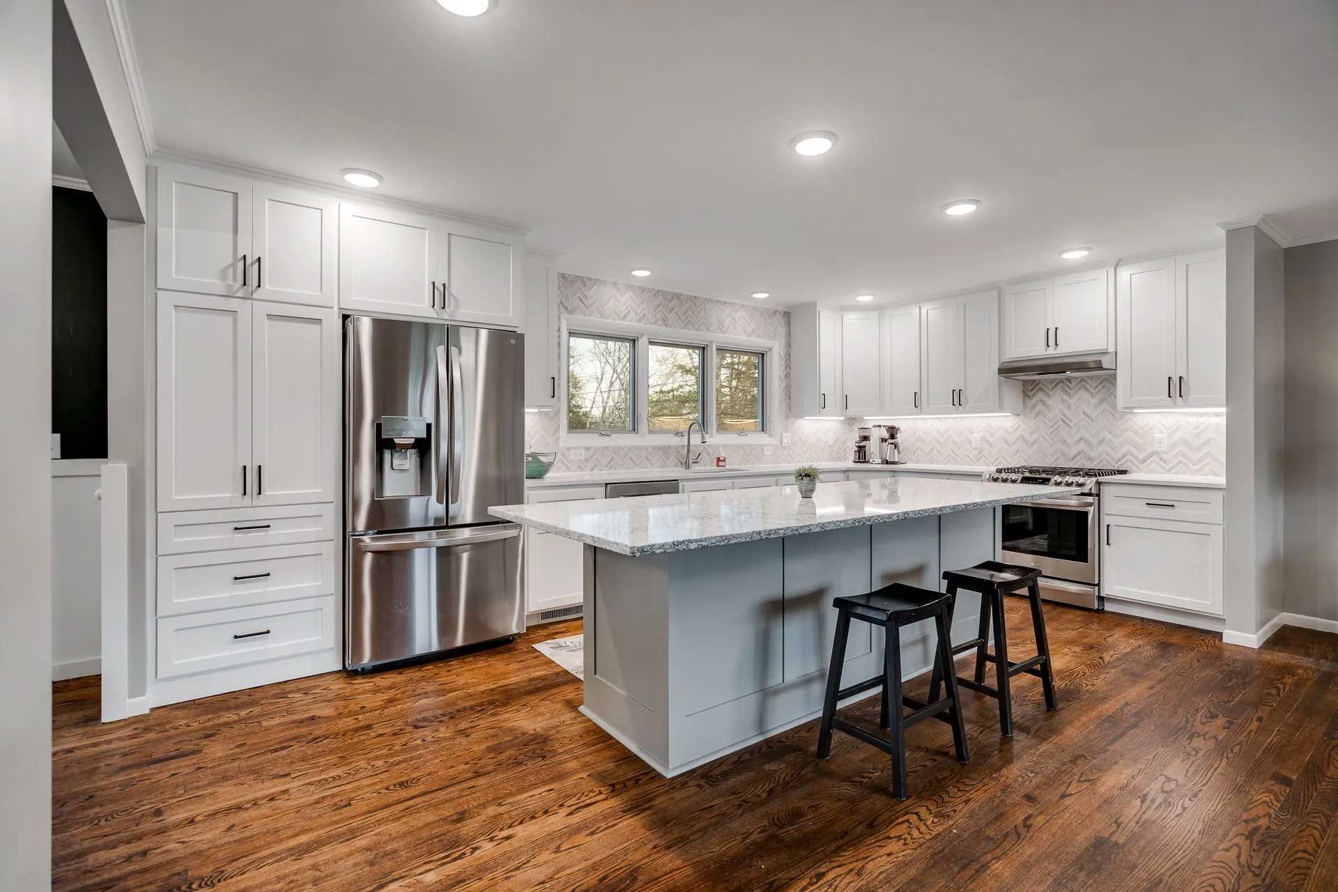 White kitchen with island, stainless steel appliances, hardwood floors, and overhead lighting.