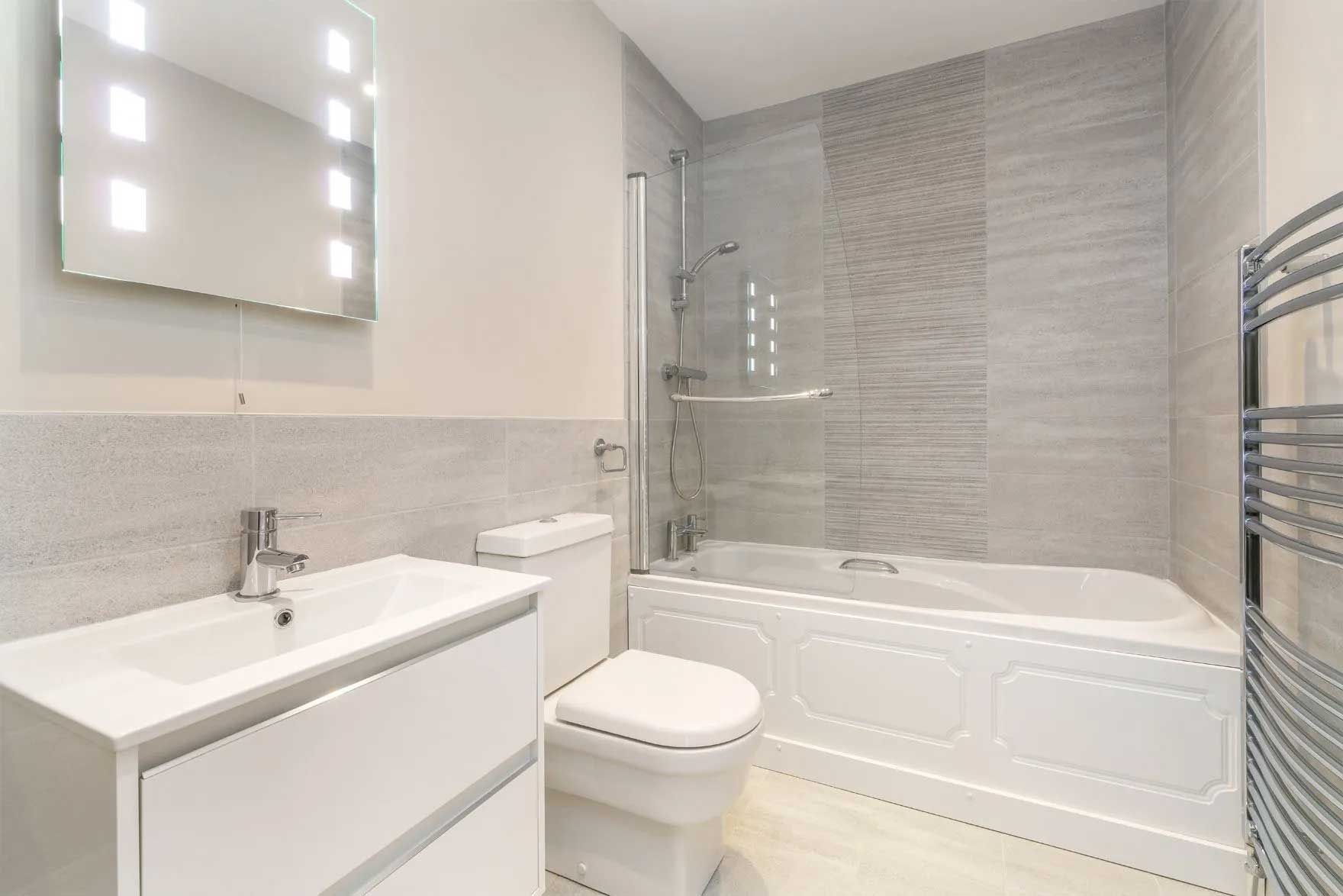Modern bathroom with white fixtures, shower-tub combo, and gray tiled walls.