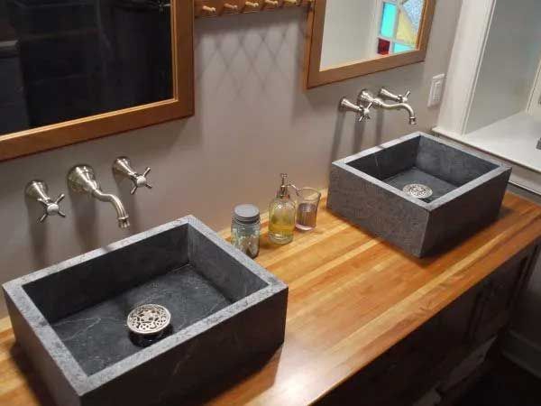 Two rectangular stone sinks with silver faucets on a wood countertop in a bathroom.