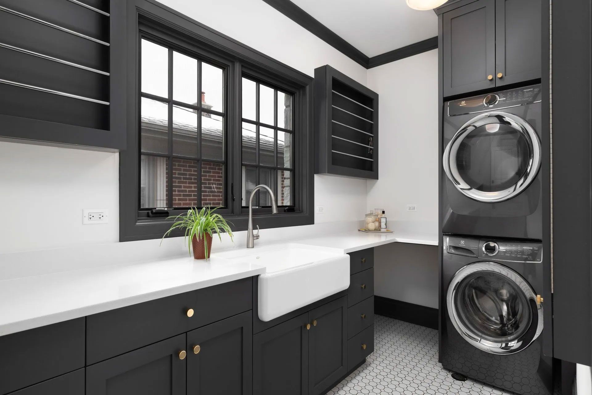 Dark gray laundry room with stacked washer/dryer, white countertops, and black window trim.