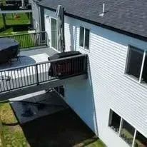 Elevated deck with a black railing connected to a two-story white house with black roof.