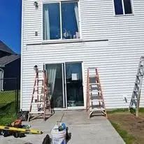 Two ladders leaning against a white house with a sliding glass door.