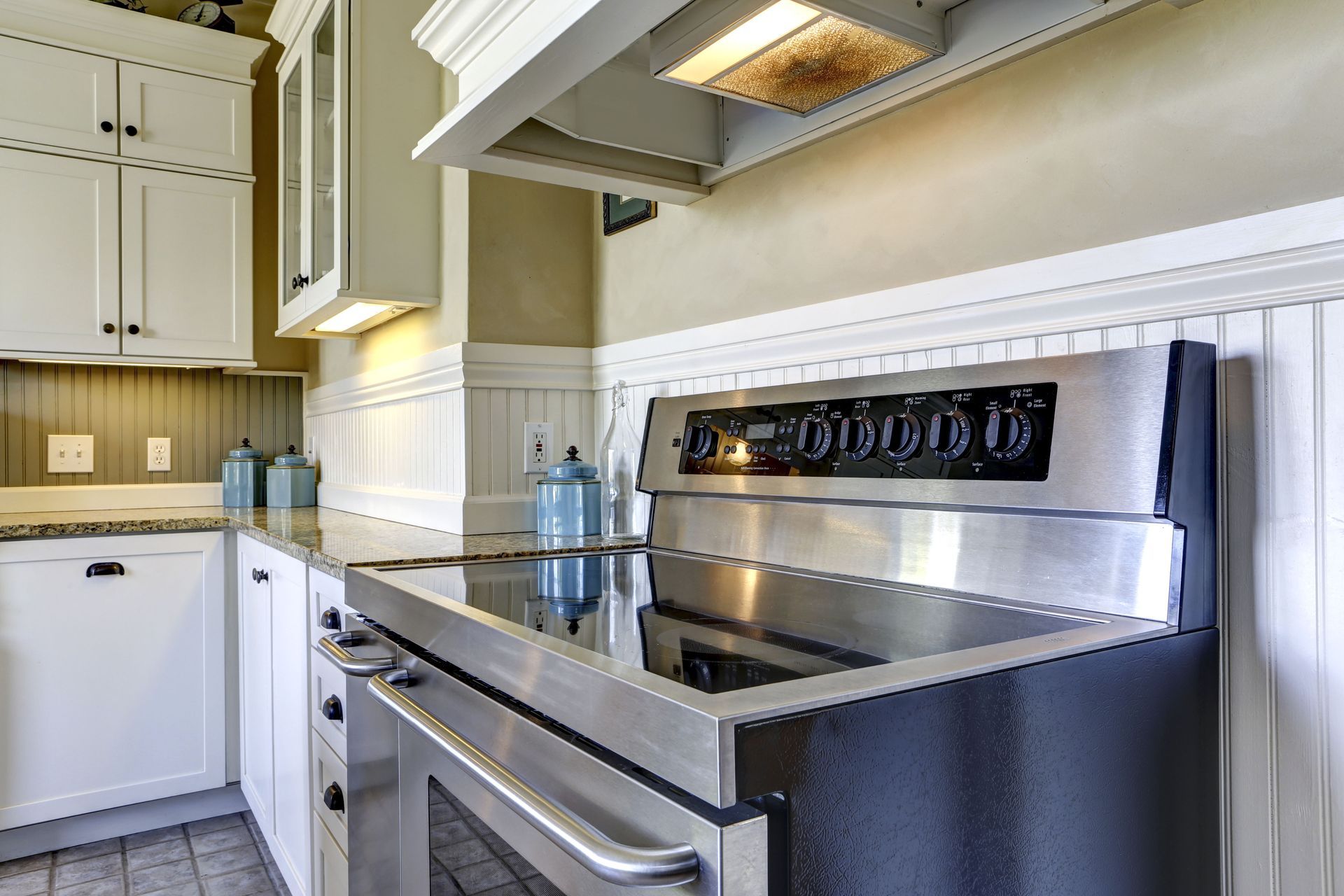 Stainless steel oven and stovetop in a bright kitchen with white cabinets, light walls, and granite countertops.